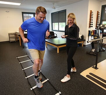 A man is running through an agility ladder drill while a therapist is beside with a stopwatch